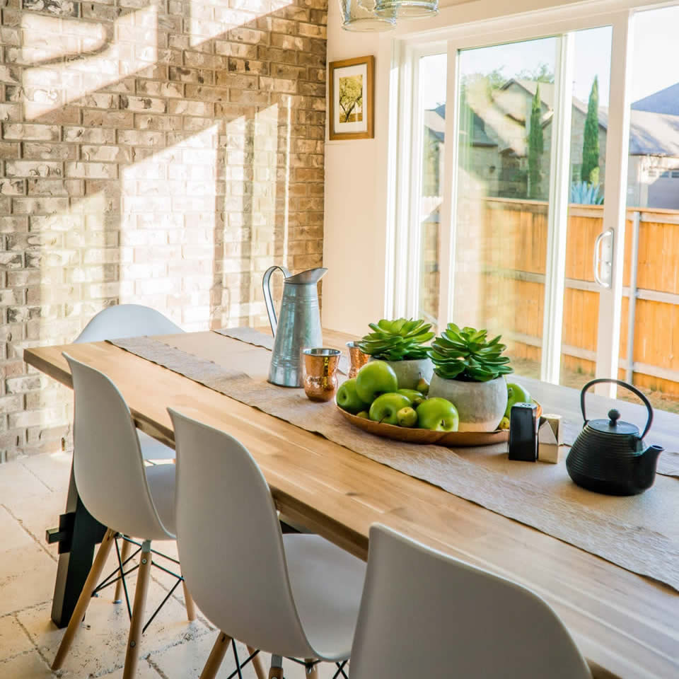 A sunny dining room containing a wooden table, chairs, and fruit on the table